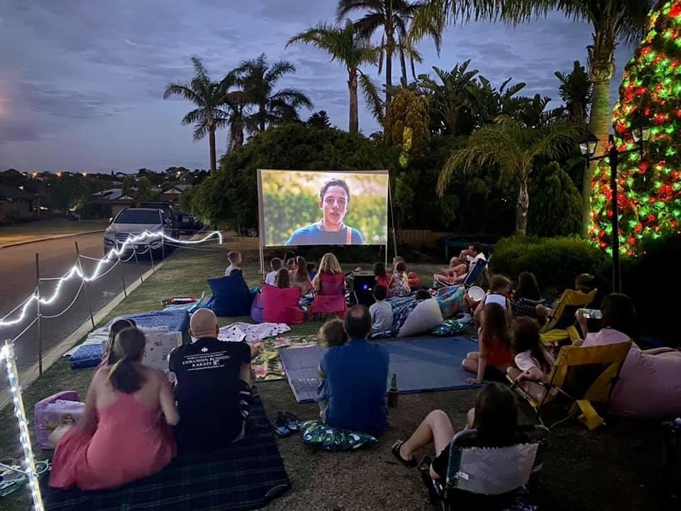Group of people watching an outdoor cinema hired in Perth on the front lawn on a Christmas evening.