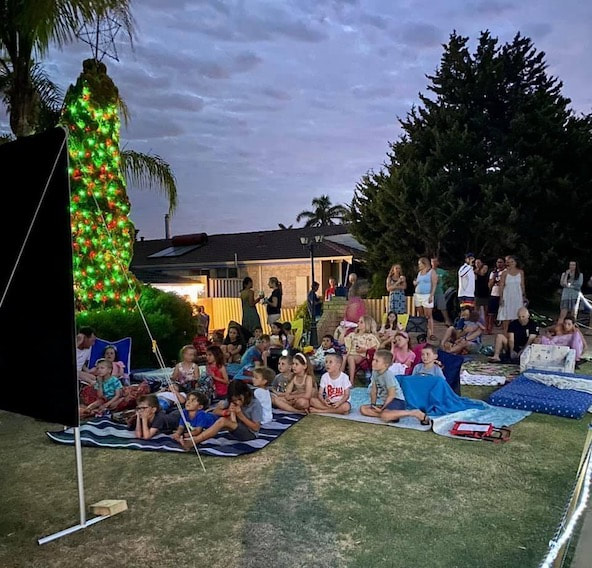 Community of people watching an outdoor cinema hired in Perth on the front lawn on a persons home.