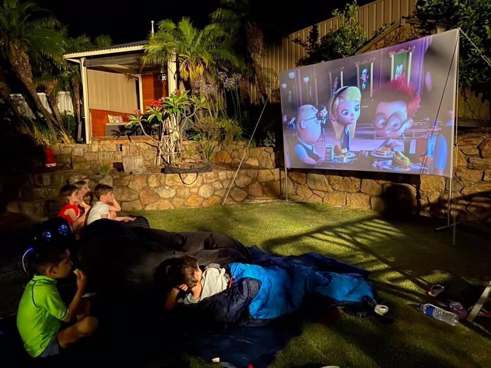 Young children in sleeping bags watching an outdoor cinema hired in Perth in their backyard.