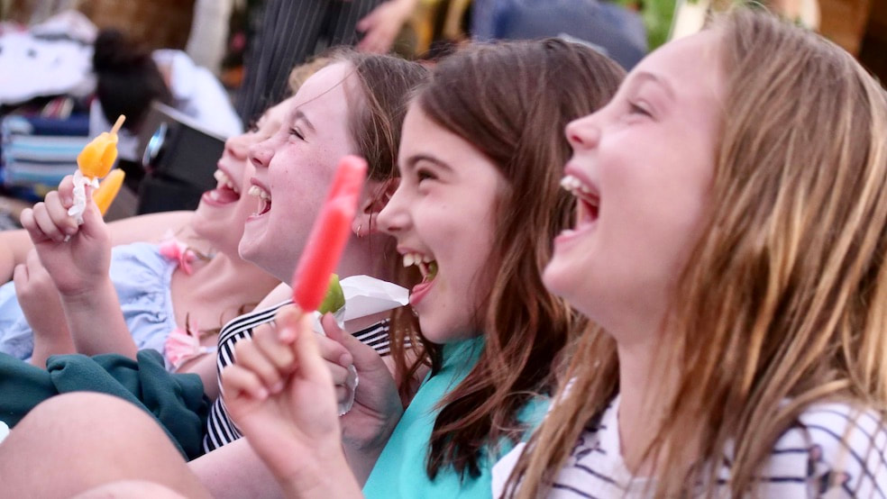 Four girls laughing while watching and outdoor cinema hired in Perth and eating ice creams.